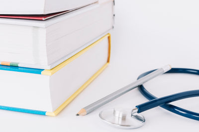 stacked books pencil stethoscope white surface